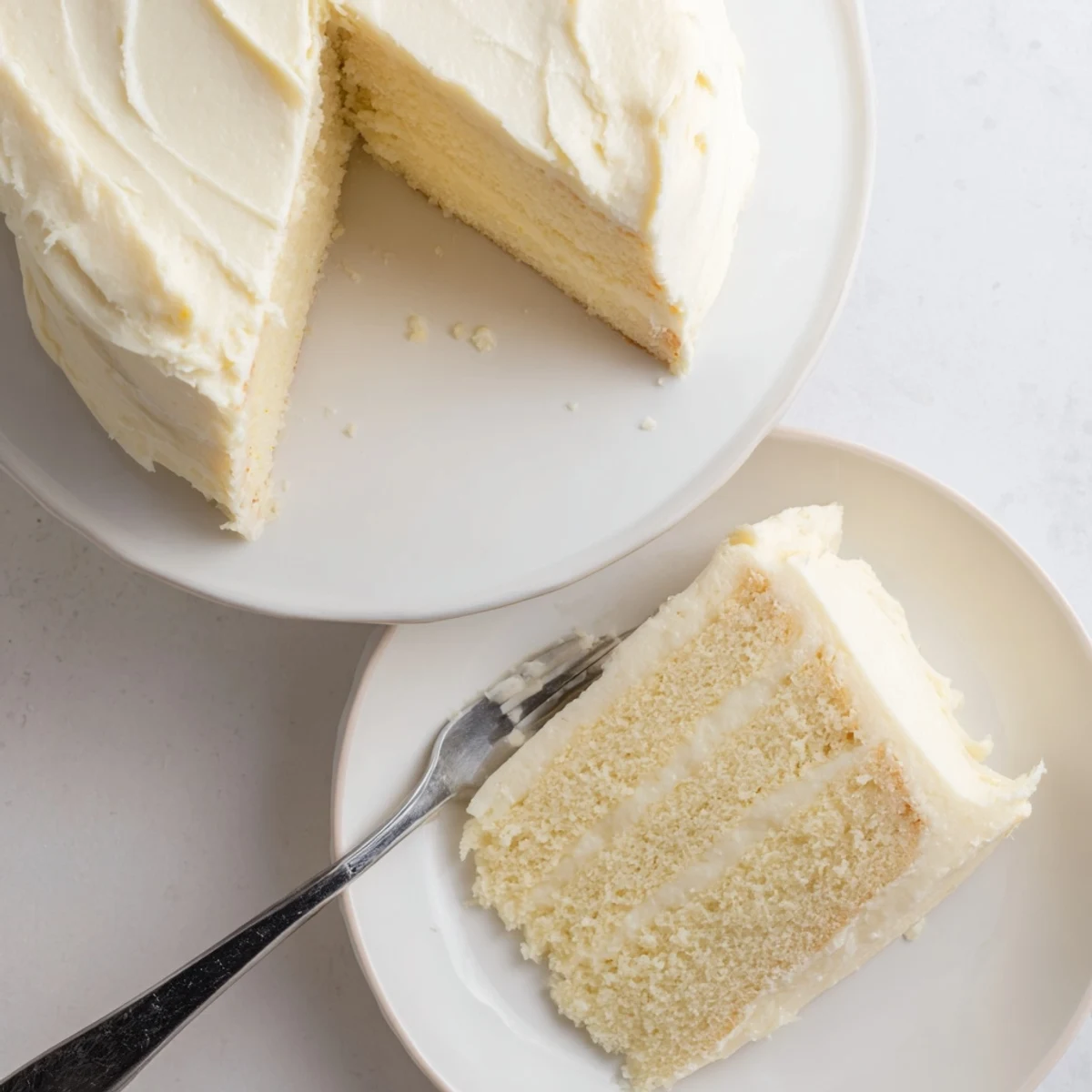 Golden slice of perfect vanilla cake revealing moist layers with creamy buttercream frosting on a white plate