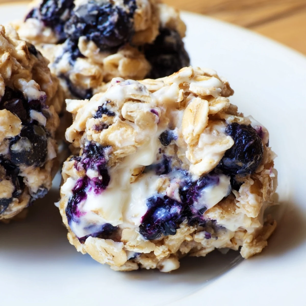 Golden blueberry cheesecake protein bites arranged on a white plate with fresh blueberry garnish