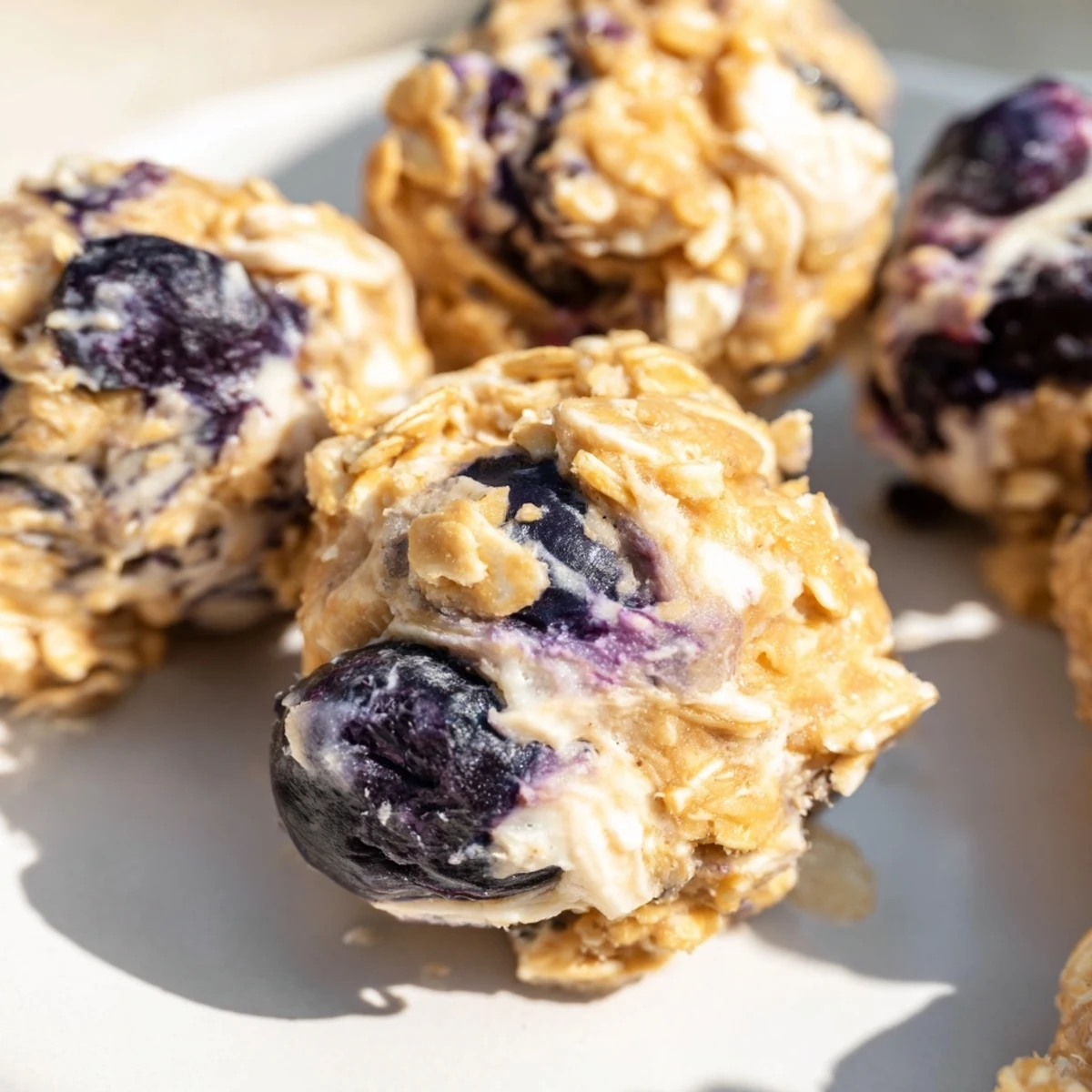 No-bake blueberry cheesecake protein bites stacked on parchment paper with lemon zest sprinkle