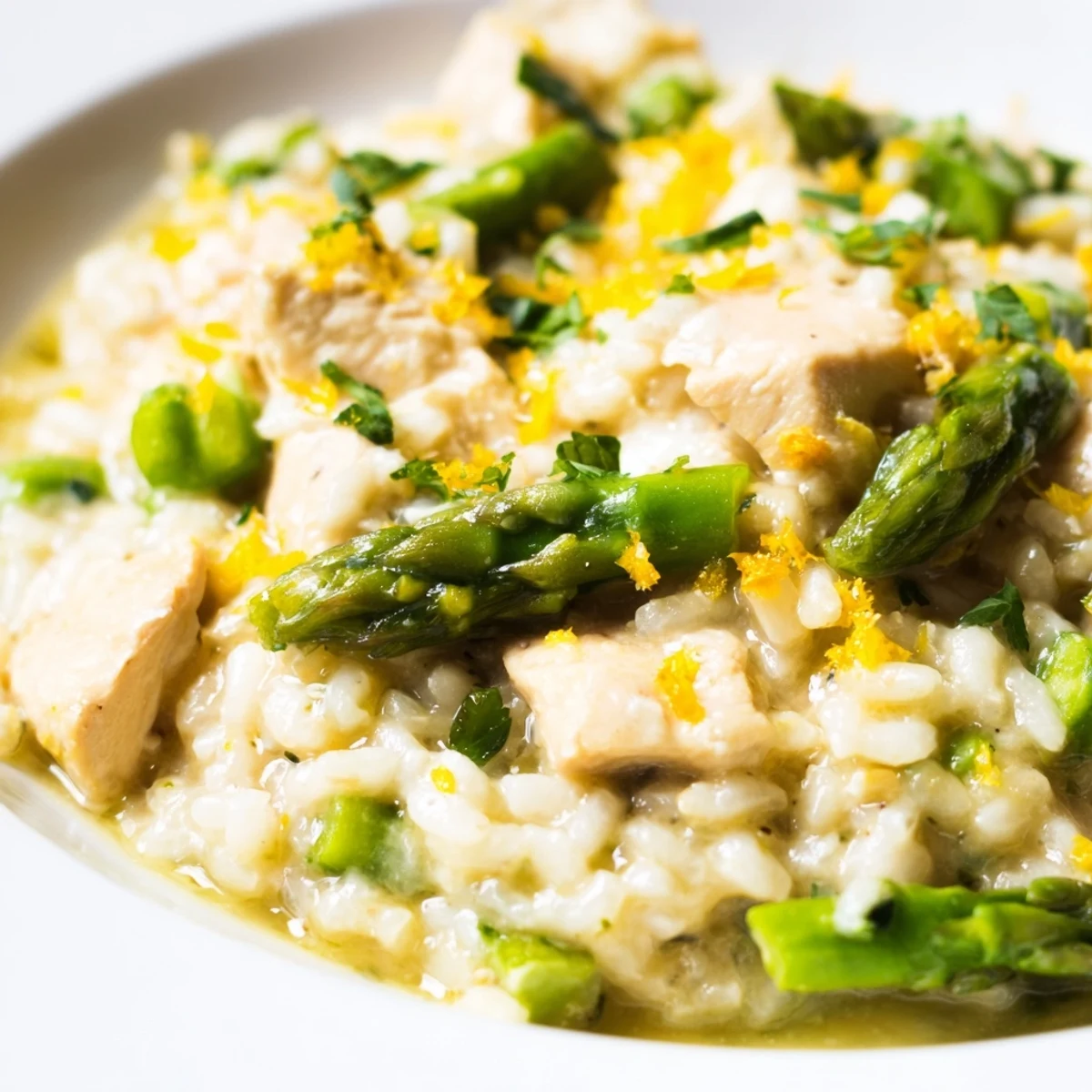 Creamy chicken and asparagus risotto topped with grated Parmesan and fresh parsley in a white bowl