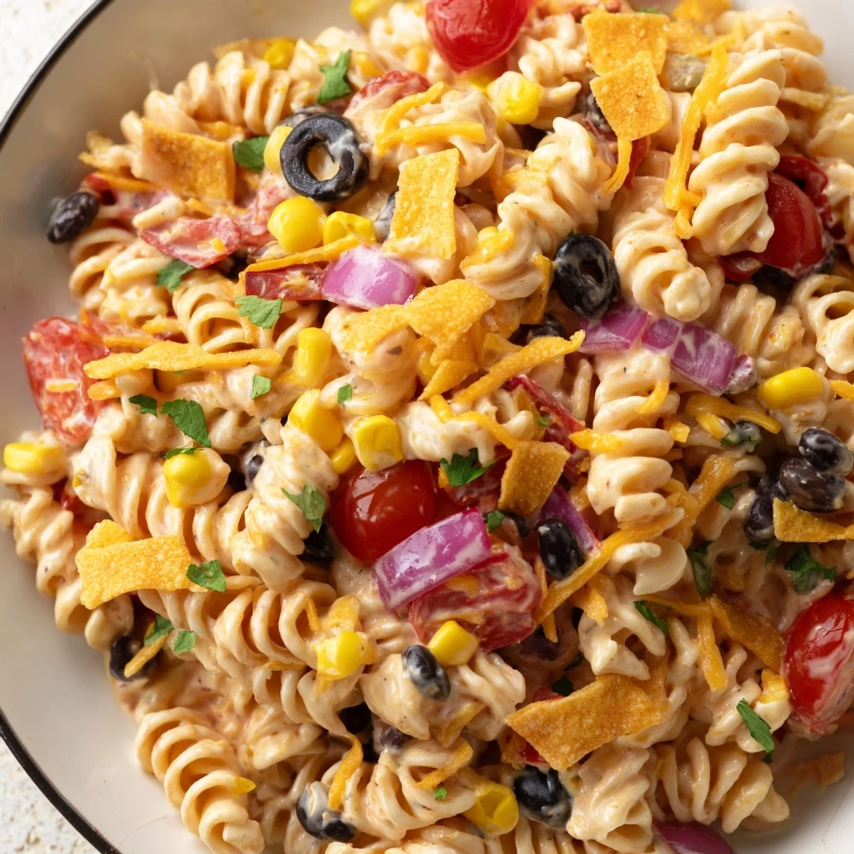 Creamy taco pasta salad topped with crushed tortilla chips, fresh cilantro, and melty Mexican blend cheese