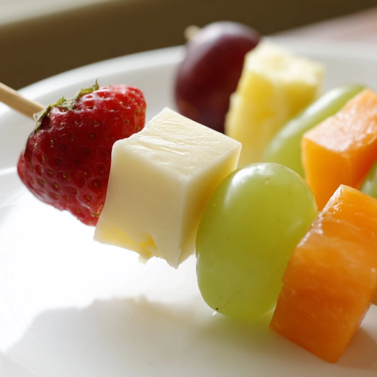 Colorful fruit and cheese kabobs arranged on a platter with grapes, strawberries, pineapple, and cheddar cubes