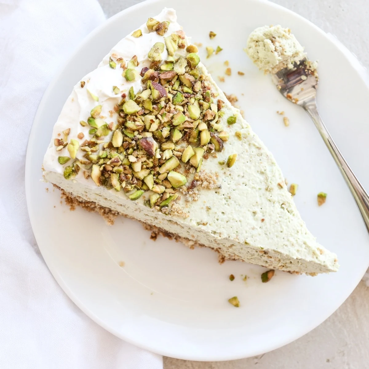 Homemade pistachio cheesecake topped with sweetened whipped cream and chopped pistachios for garnish