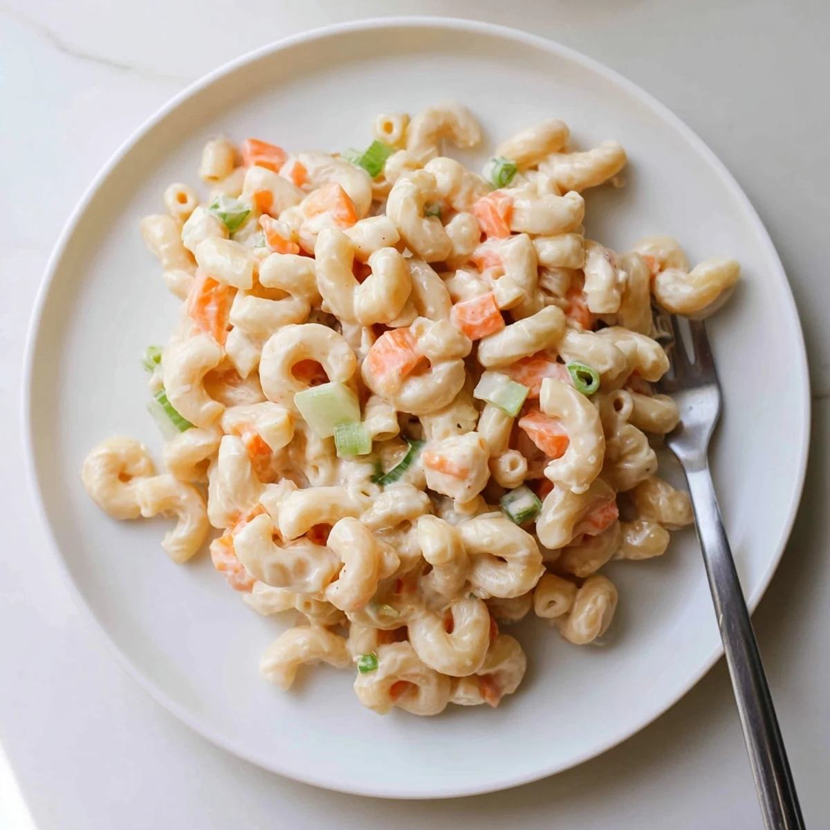 Close up of Hawaiian style mac salad showing glossy coated pasta with vibrant green onions and orange carrot bits
