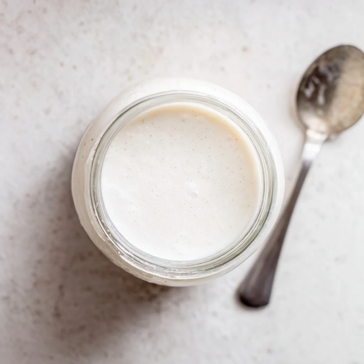 Fresh batch of dairy-free almond milk pouring into clear glass on wooden counter