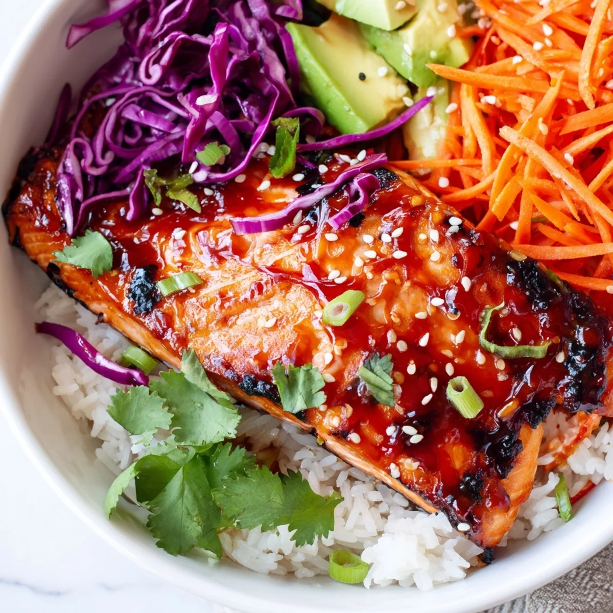 Caramelized salmon resting on fluffy rice with crisp cabbage, carrots, and creamy avocado slices