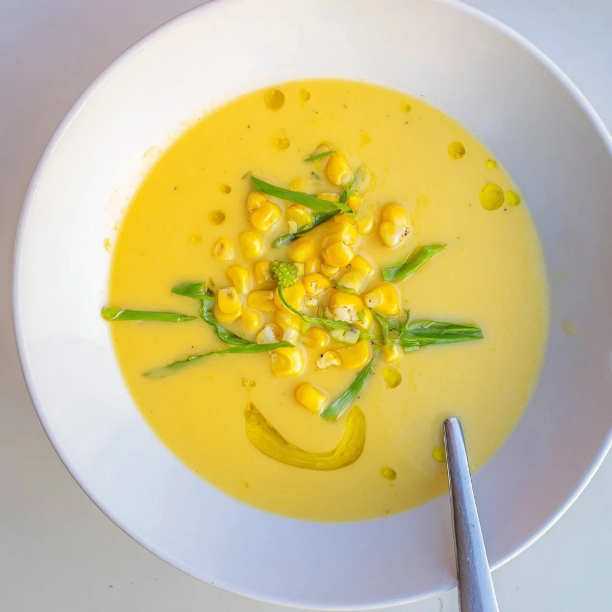 Bright yellow summer sweet corn gazpacho poured into shallow bowls with fresh herb sprinkles