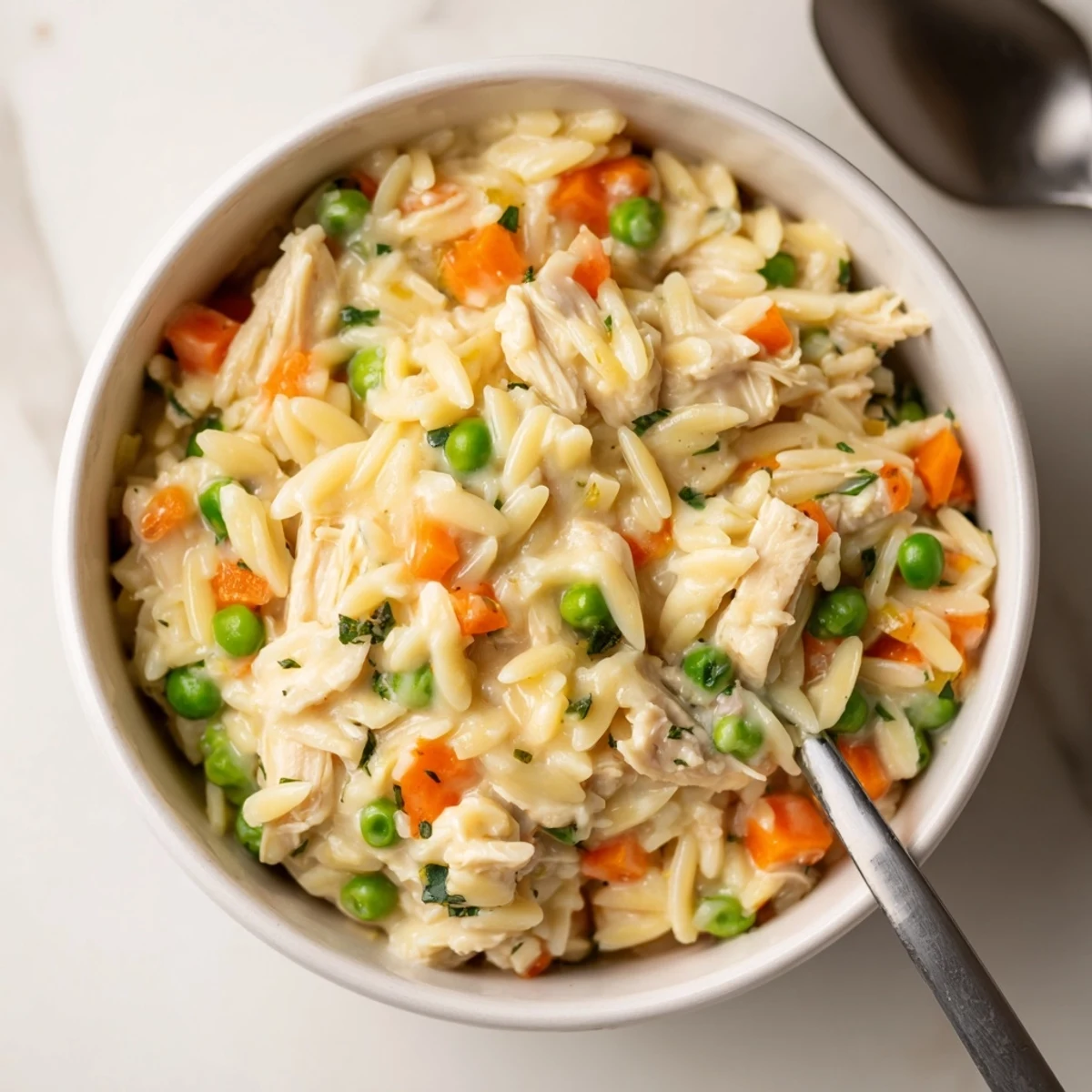 Bowl of creamy chicken pot pie orzo garnished with fresh parsley showing a thick and luscious texture.
