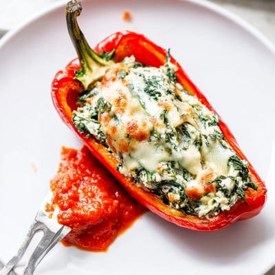 Creamy ricotta stuffed peppers nestled in rich tomato sauce on a white plate